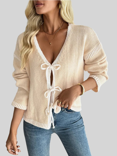 Beige knit cardigan with white trim, V-neck and tie-front bows, styled with jeans.