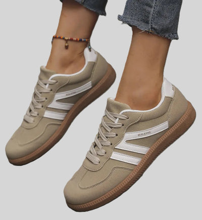 Beige sneakers with white side stripes and gum brown sole, laced up and worn with jeans.