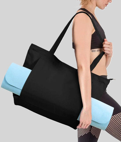 Black gym tote with a blue yoga mat peeking out, carried by a woman in workout gear.