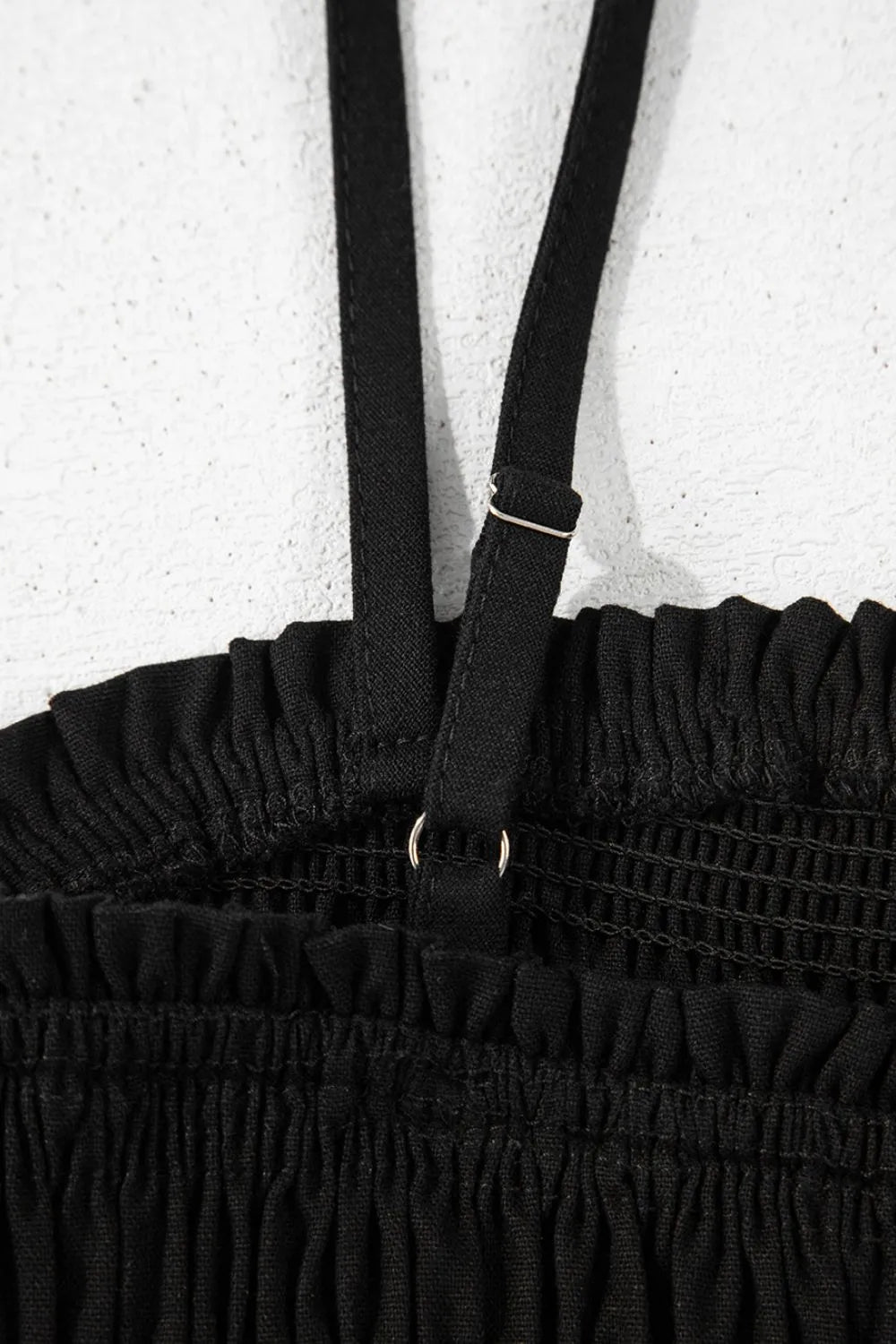 Black smocked wide-leg jumpsuit close-up of adjustable spaghetti straps and gathered waist