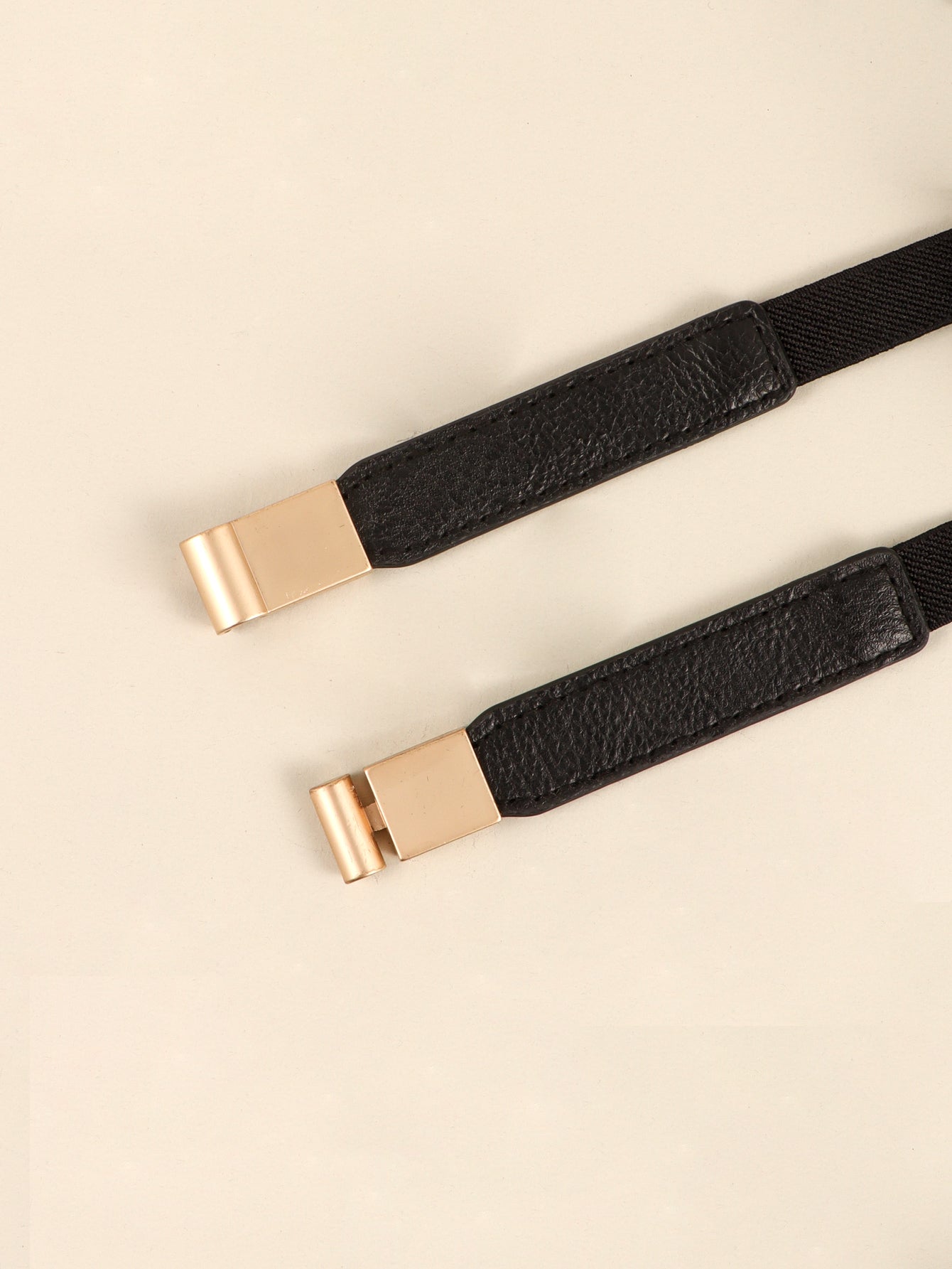 Black elastic skinny belt with gold-tone buckle close-up detail