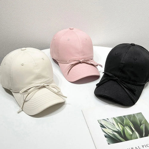 Solid color baseball caps in blush pink, cream, and black with bow ties