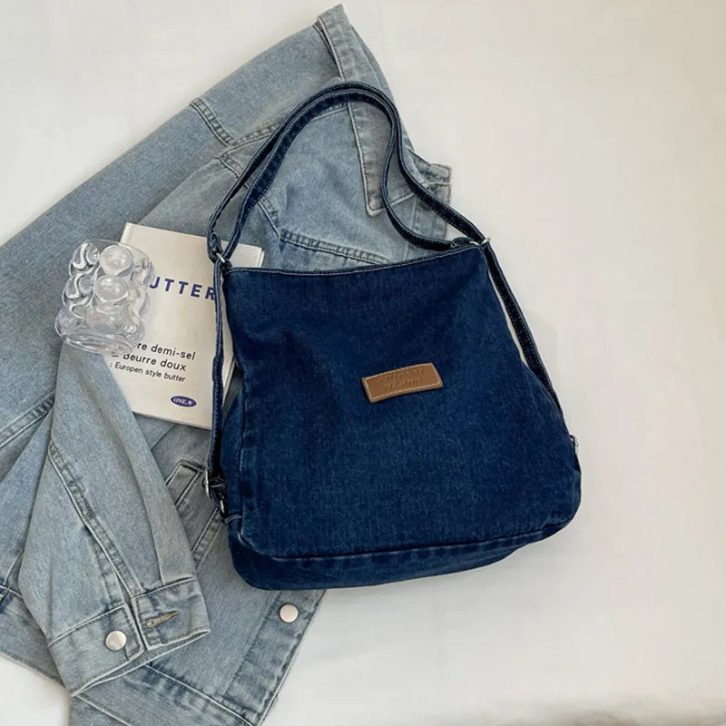 Blue denim shoulder bag with adjustable strap and rectangular leather logo patch