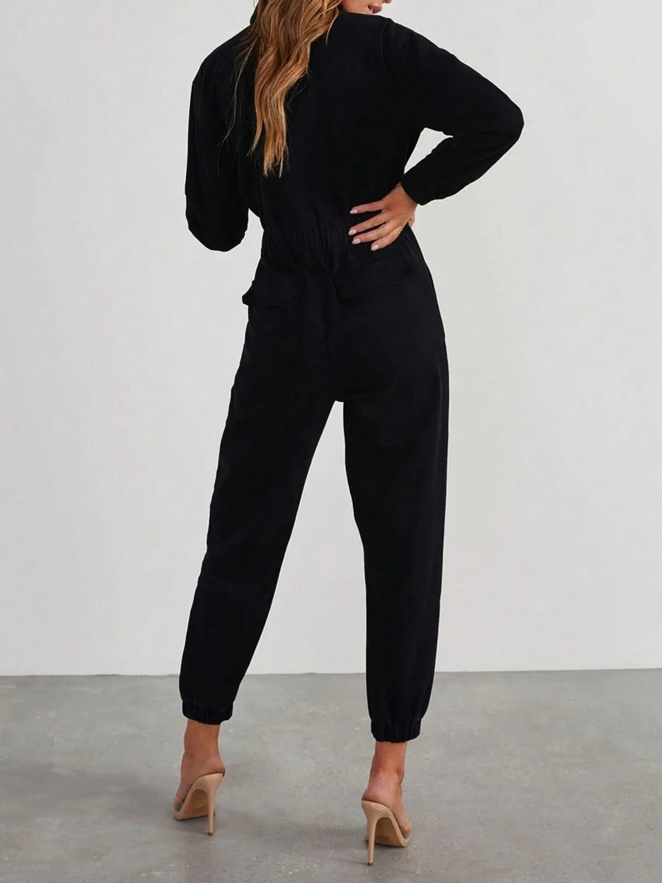 Black long-sleeve zip-front jumpsuit, back view with drawstring waist and cuffed legs