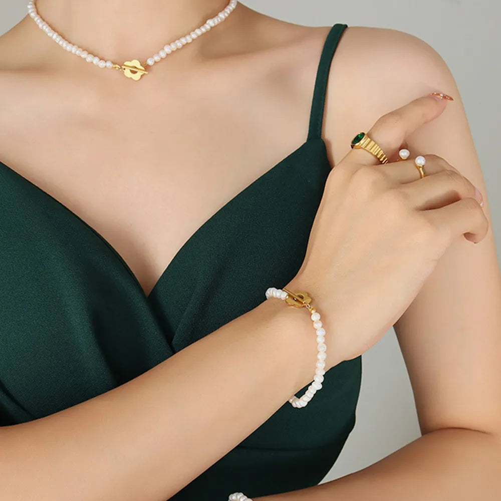 Pearl bead bracelet with gold flower charm on wrist, styled with rings