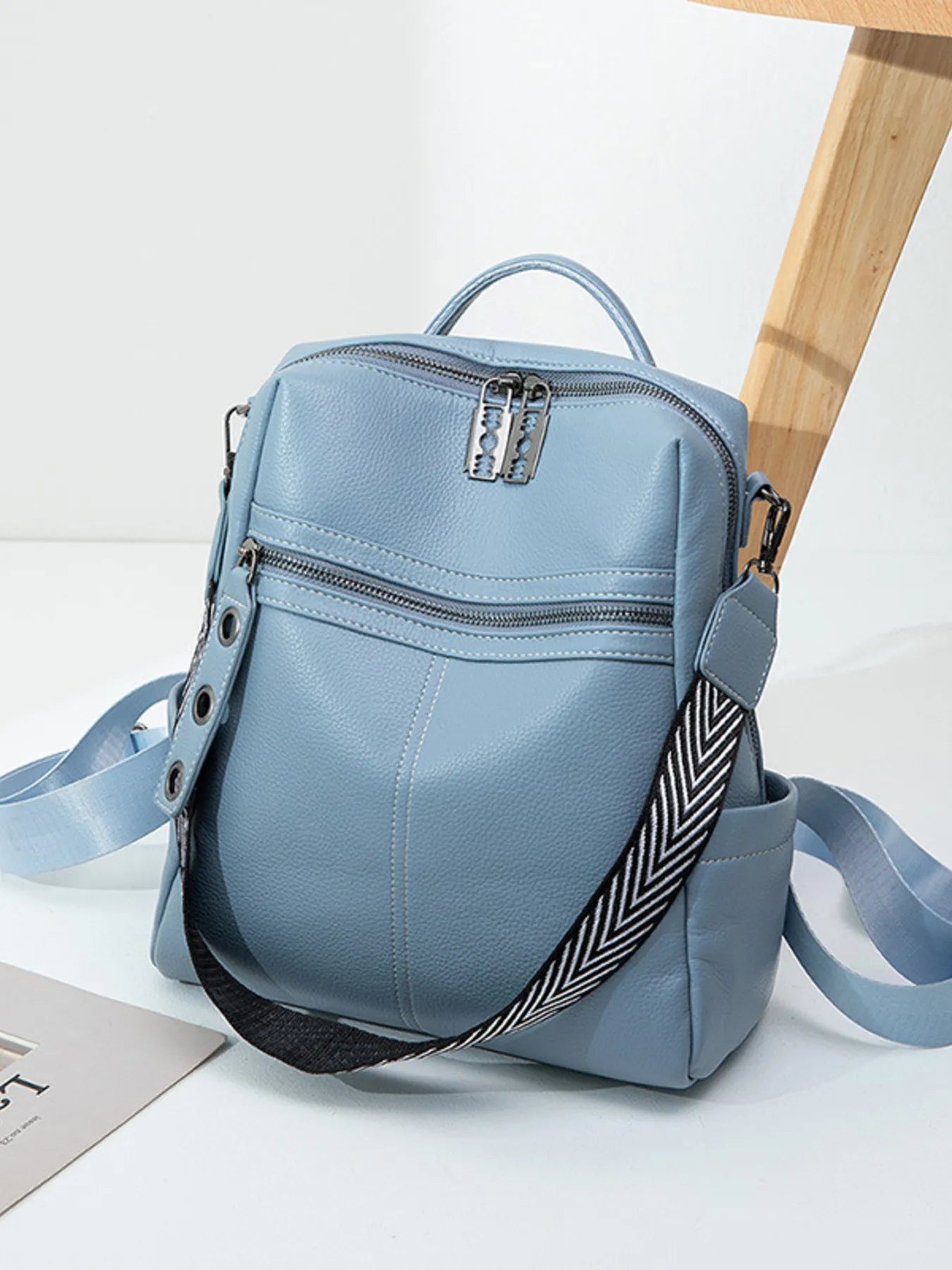 Light blue leather backpack bag with front zip pocket, top handle, adjustable strap