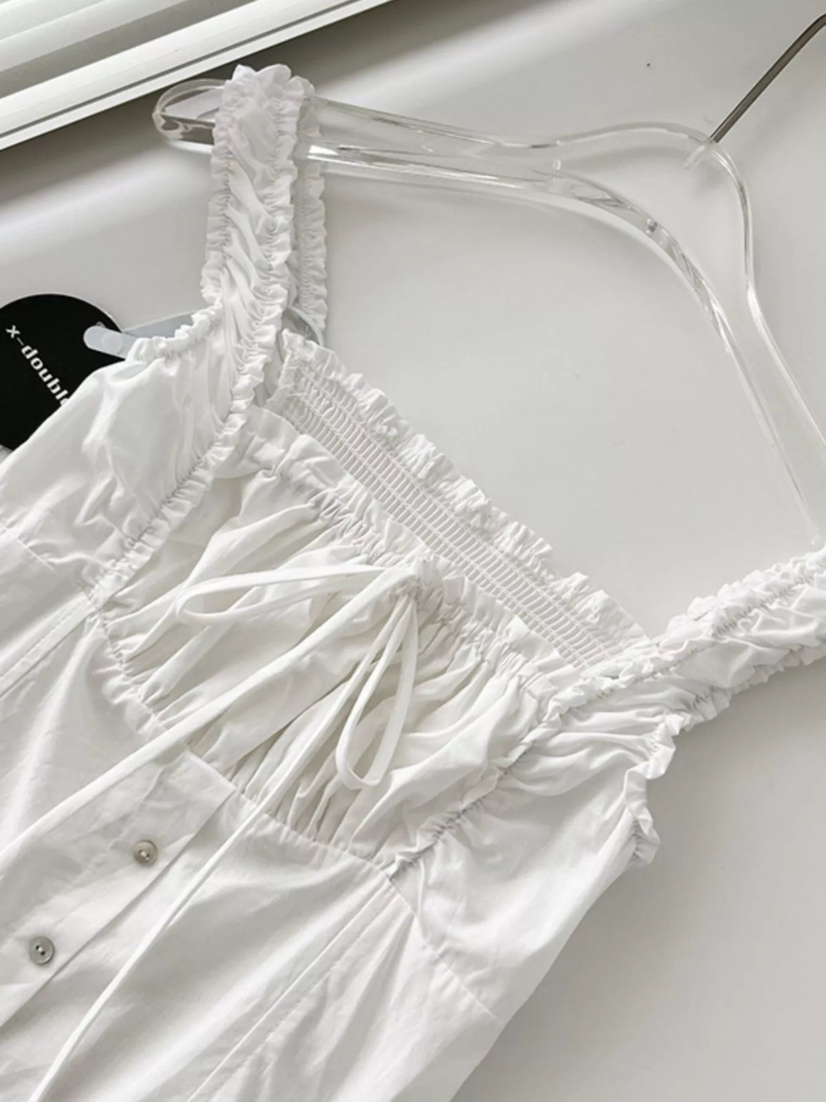 White cotton dress detail: smocked square-neck bodice with ruffled trim and tie laces