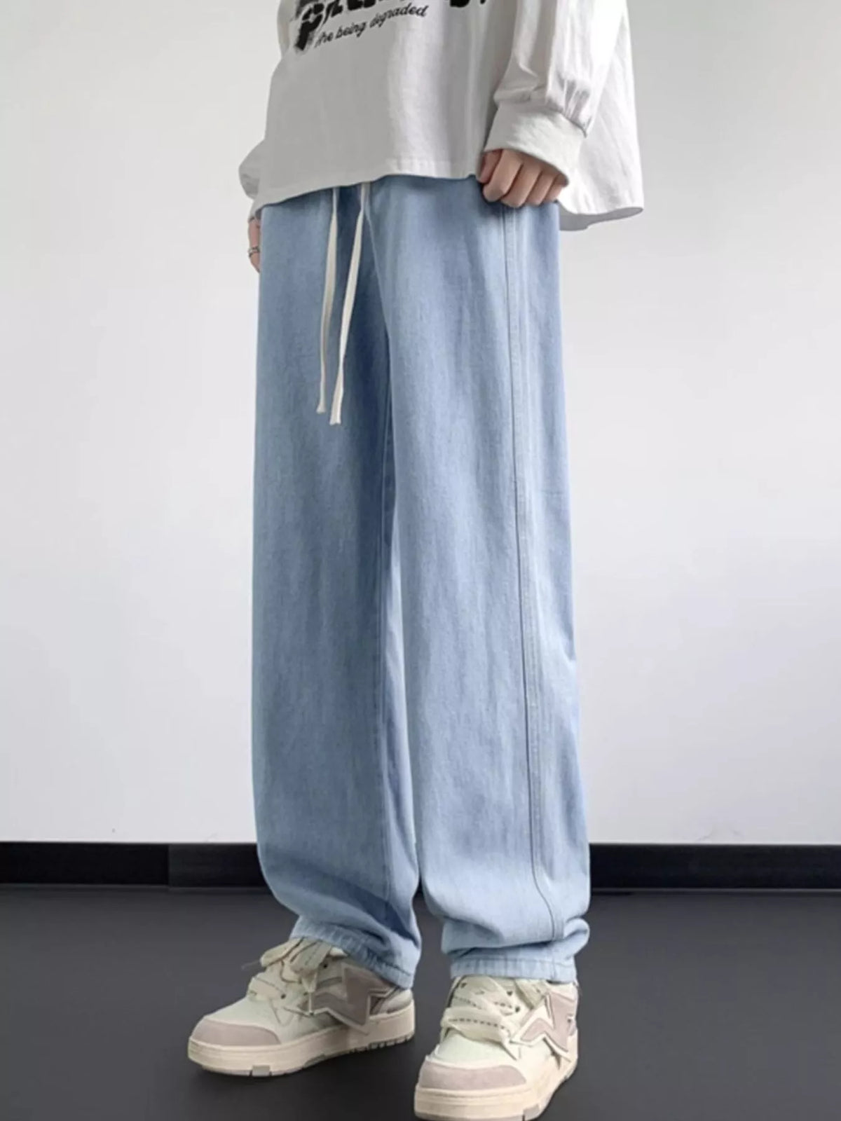 Light blue washed denim jeans with loose fit, wide legs, and front drawstring ties