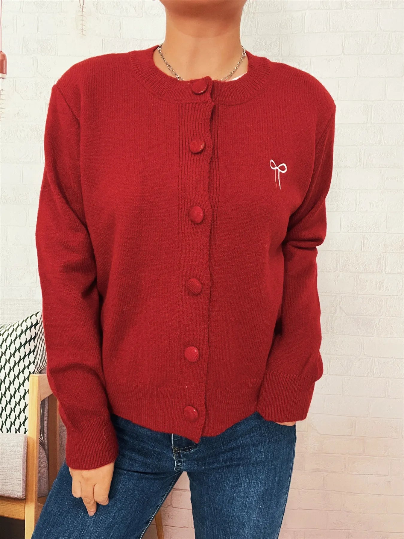 Red button-front cardigan with round neckline and bow detail on upper right chest