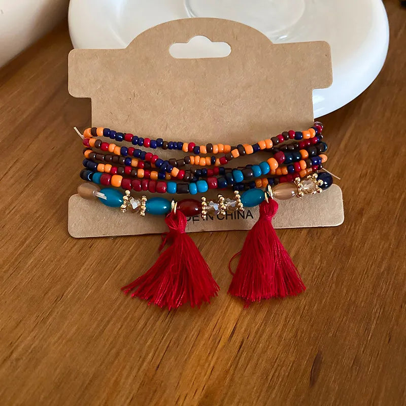 Colorful beaded tassel bracelet with red, blue, orange, and gold charms and red tassels