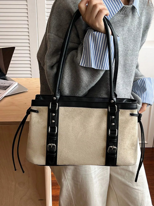 Cream and black tote bag with long straps, front buckle panel, and rivet trim