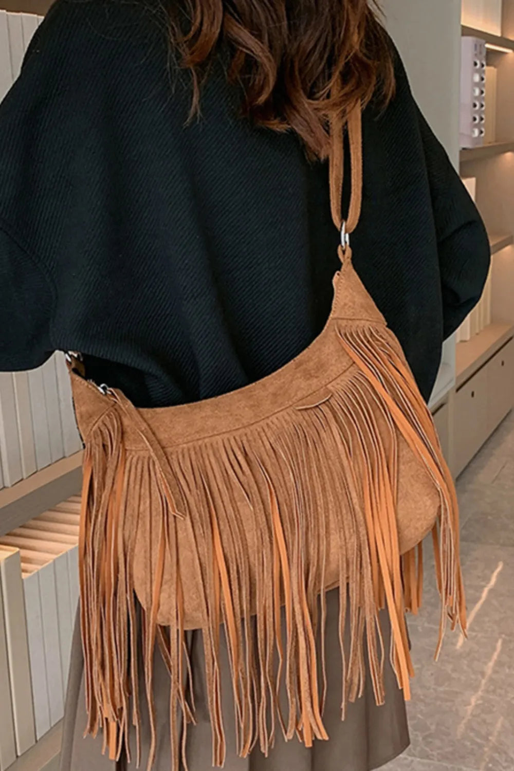 Tan suede fringe shoulder bag with adjustable strap worn over a dark top