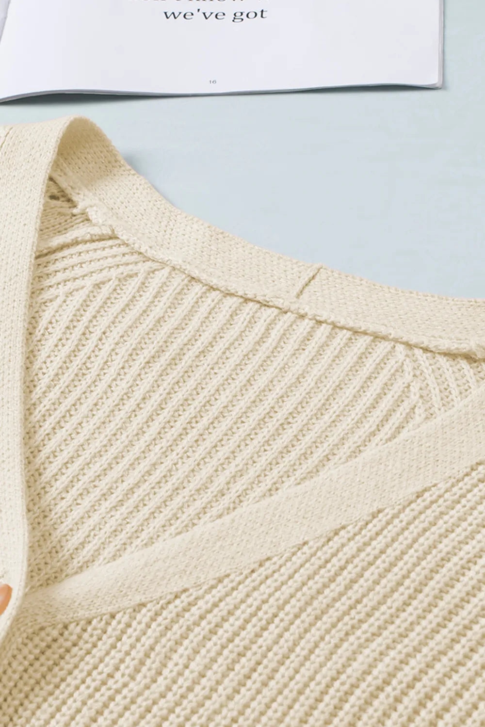 Cream knit V-neck yoke and collar detail on a button-up cardigan with ribbed trim