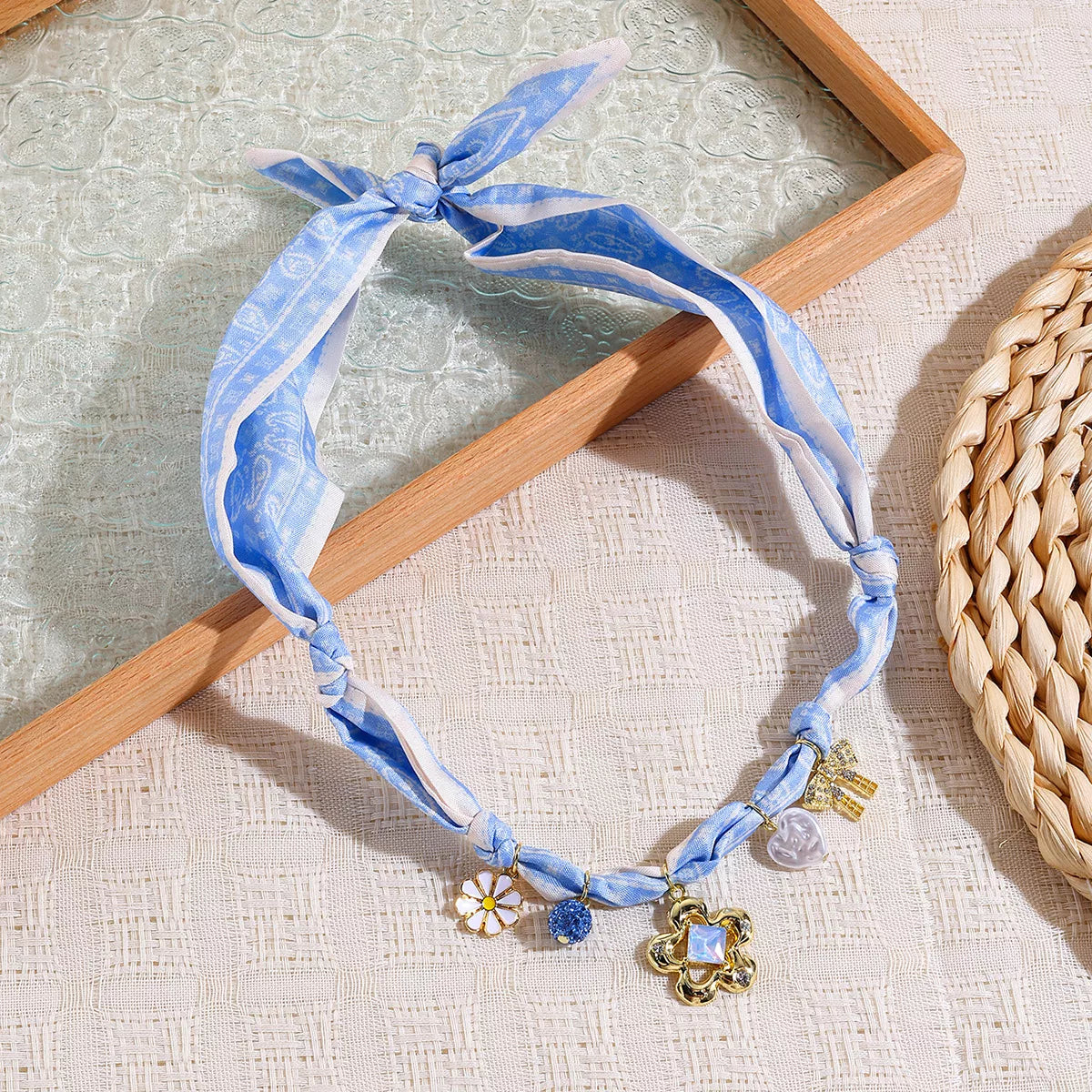 Light blue ribbon charm necklace with gold flower and crystal charms, flat lay