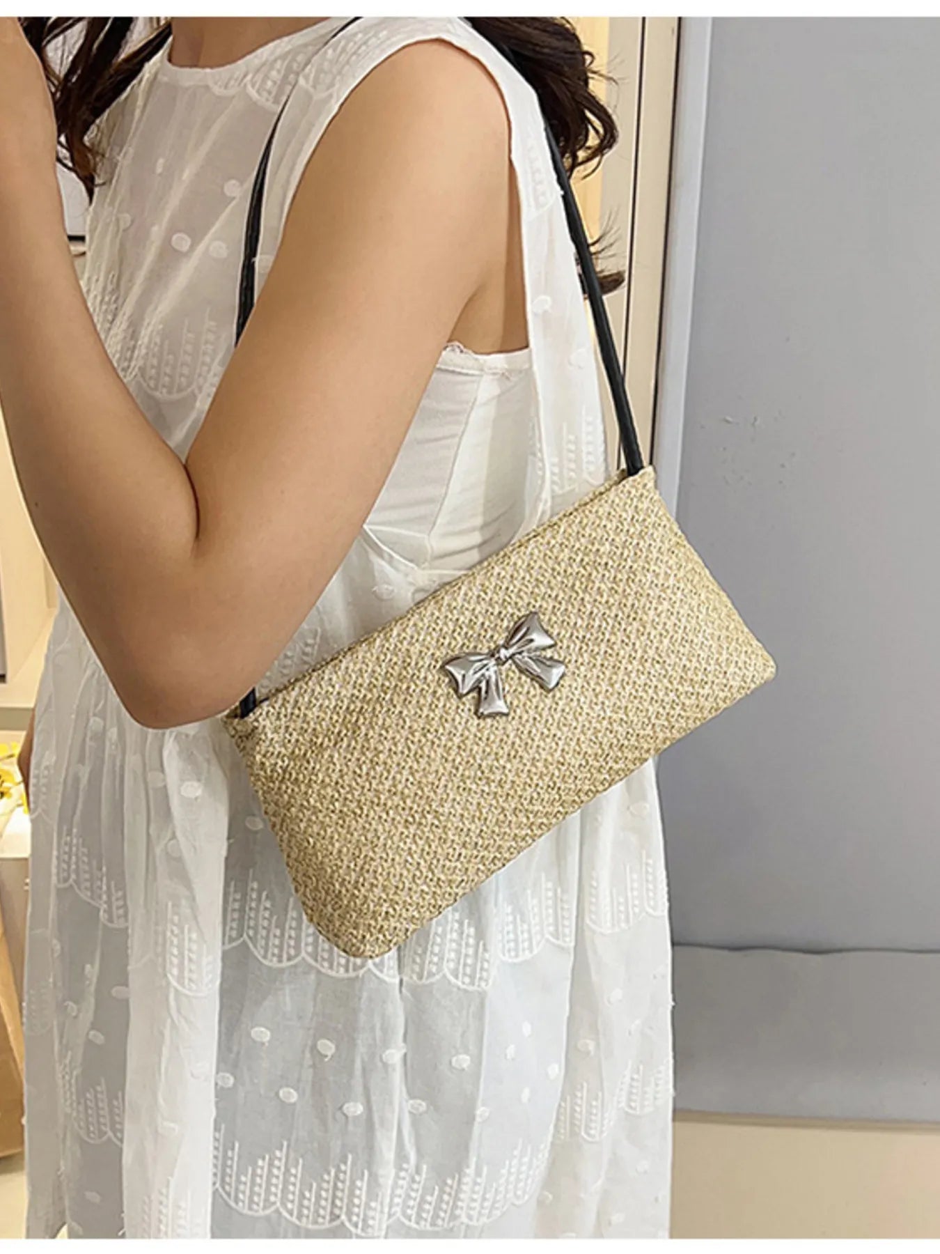Woven straw shoulder bag with silver bow appliqué and black strap, textured tan