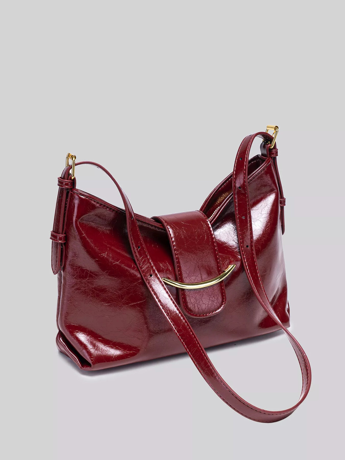 Wine red gloss vegan leather crescent shoulder bag side view with centered clasp and strap