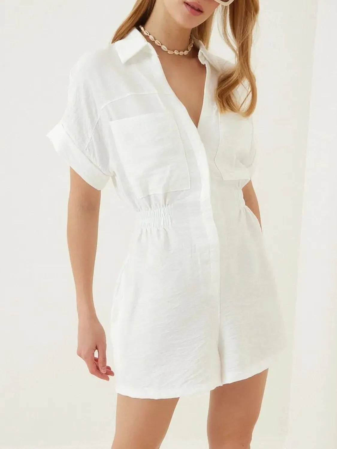White short-sleeve romper with collar, button front, patch pockets, and gathered waist seam.