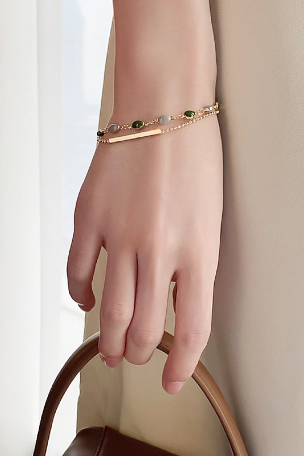 Gold-tone double-layer bracelet on hand with green and gray beads and bar detail