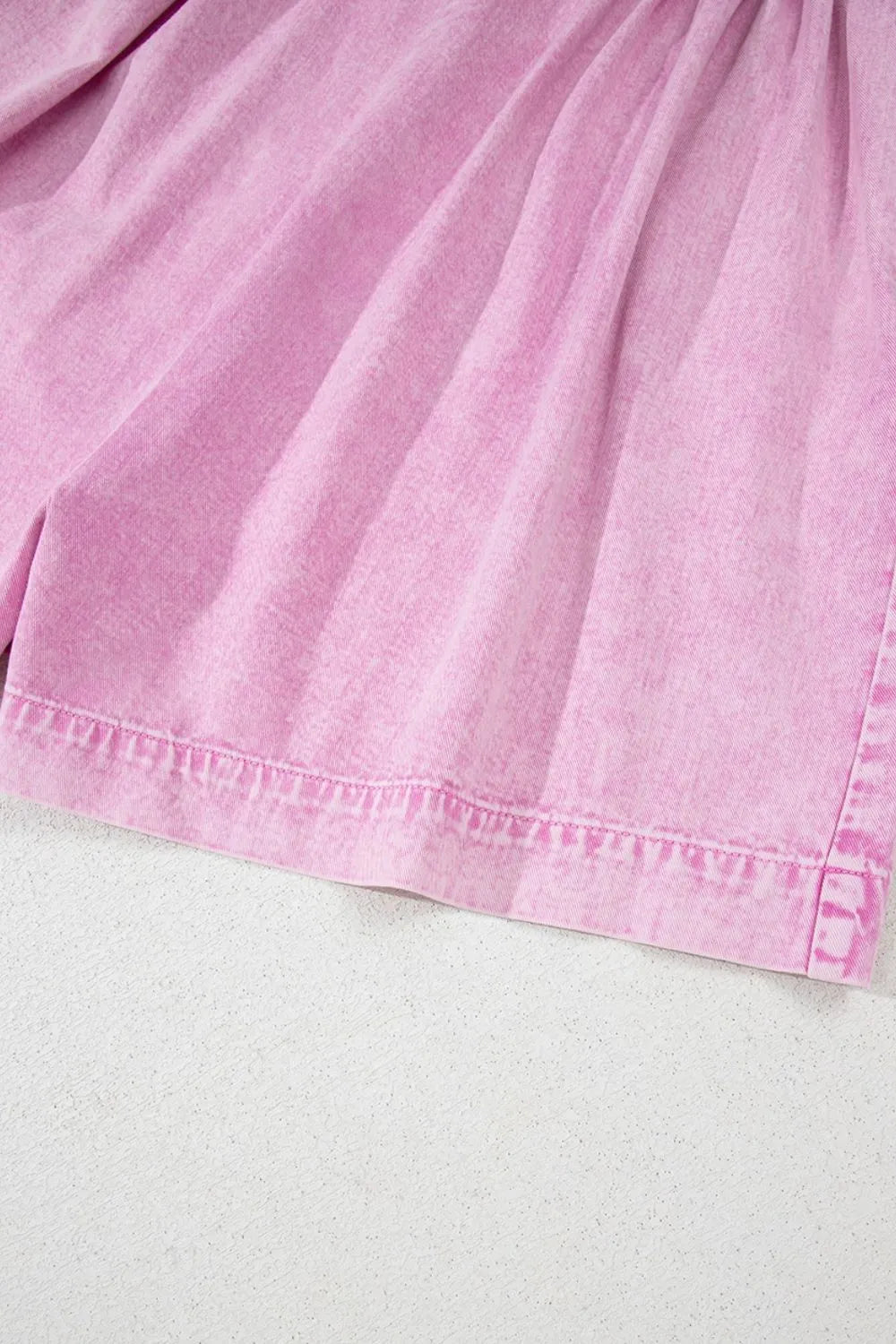 Pink mineral-wash denim romper bottom hem with gathered skirt detail