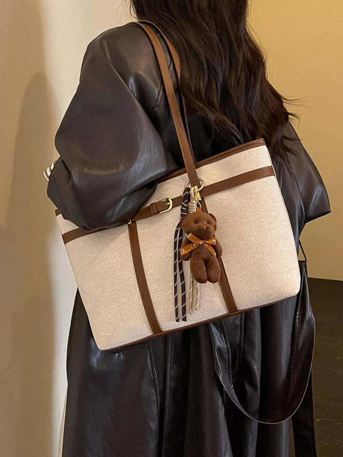 Off-white vegan leather tote bag with brown trim, long shoulder strap, and teddy charm
