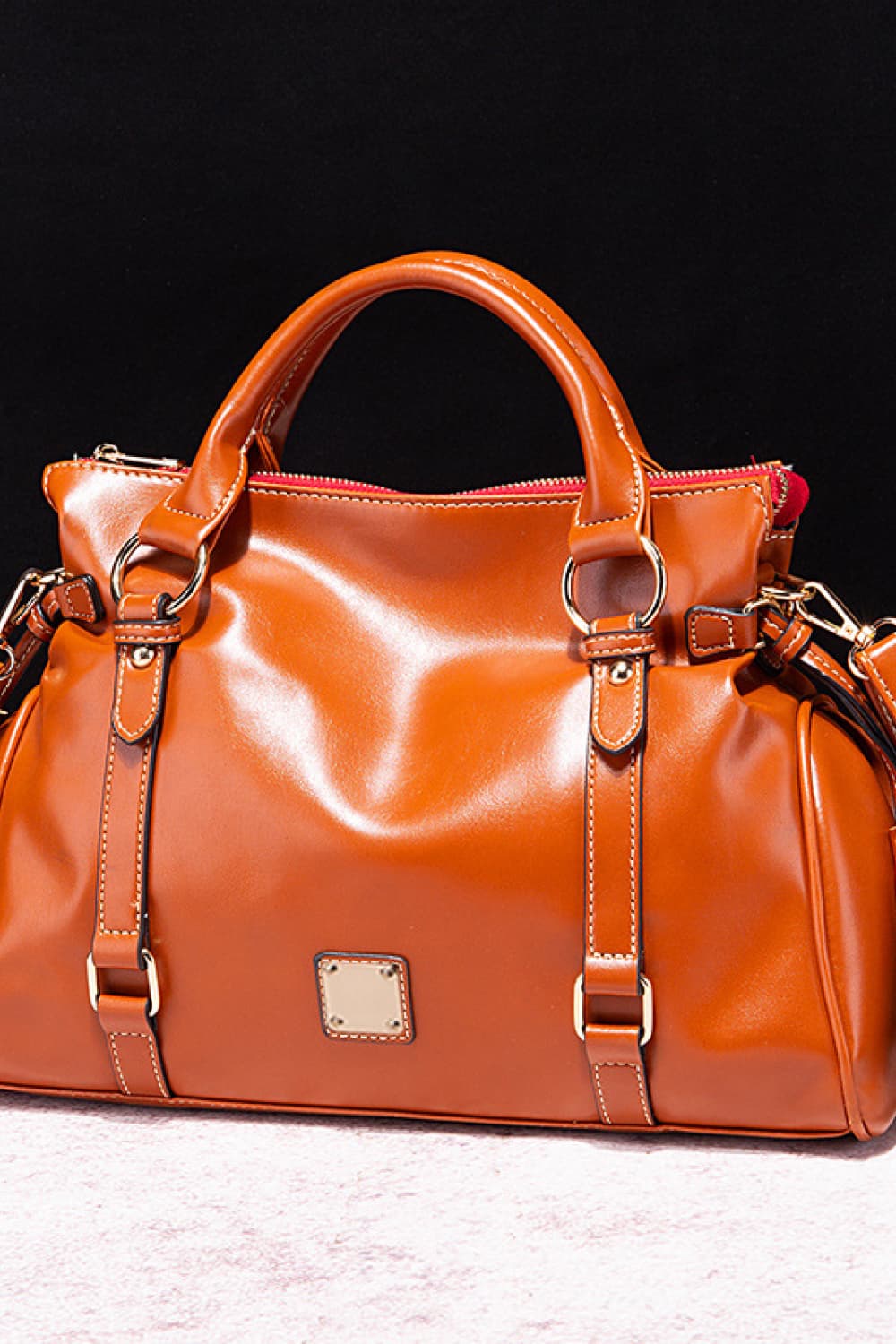 PU leather handbag in caramel orange with tassels, top handles, and front zipper pocket.