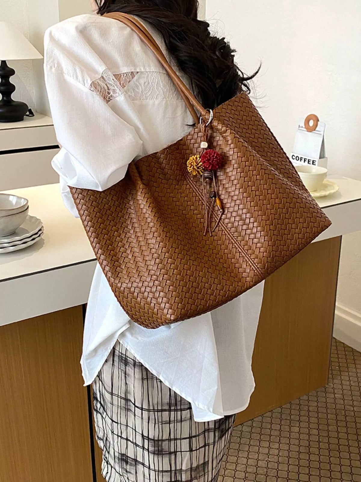 Brown woven vegan leather tote bag with long handles, zipper top, and floral tassel charm