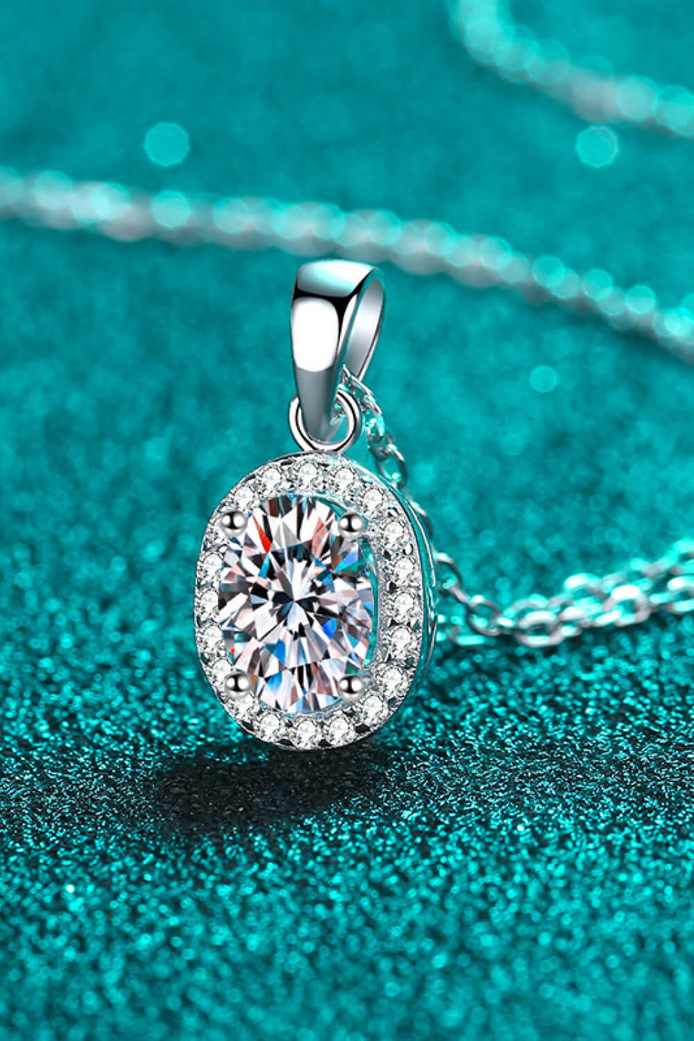 Silver oval moissanite pendant with sparkling halo, close-up on chain