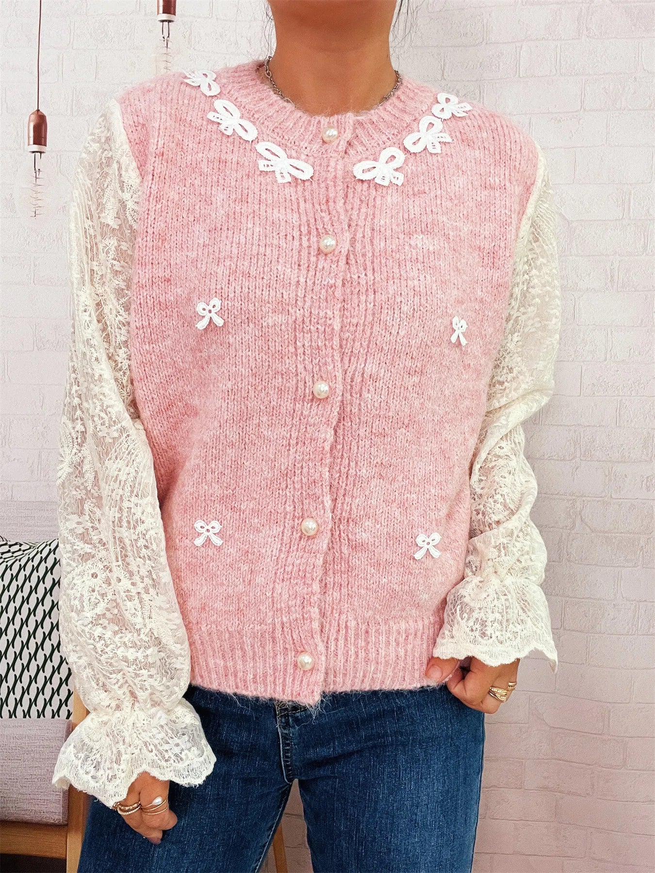 Pink knit button-up cardigan with lace sleeves and white bow accents, front view