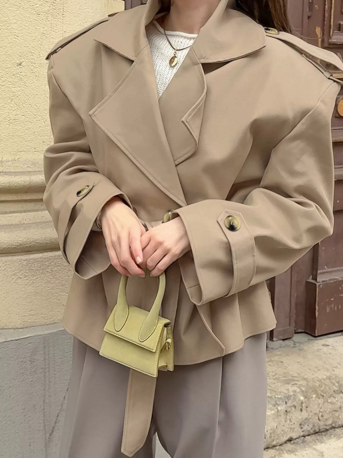 Khaki belted trench coat with wide lapels, gold buttons, and cuff details