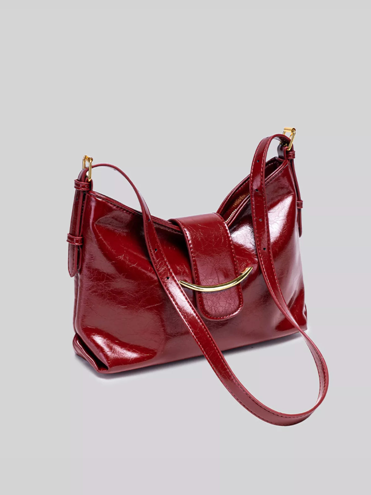 Wine red gloss vegan leather crescent shoulder bag angled view with centered clasp