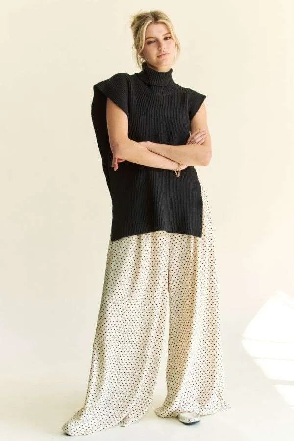 Black sleeveless turtleneck knit top with side slit, worn over patterned pants