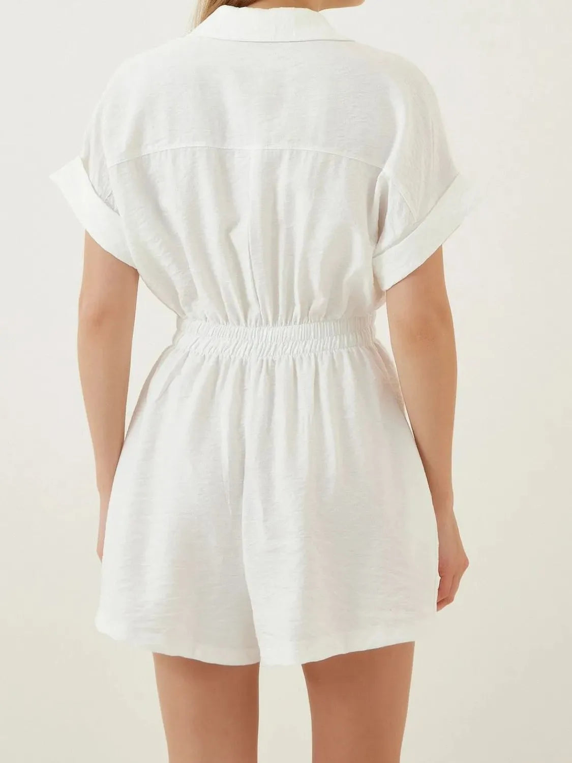 Back view of white short-sleeve romper with collar and cinched elastic waist.