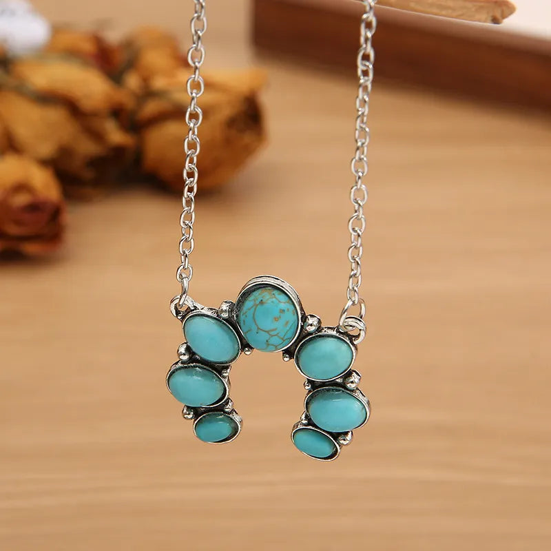 Turquoise oval stone pendant necklace on silver-tone chain, cross-like clustered pendant.
