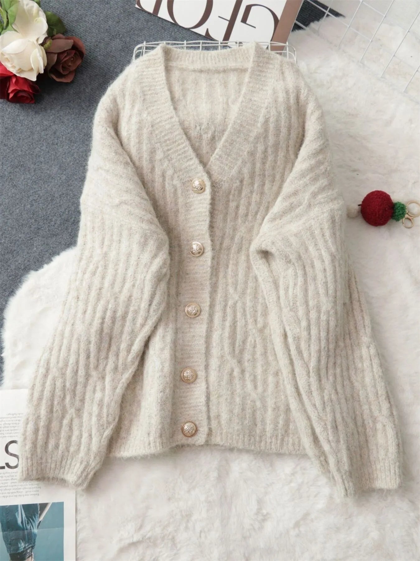 Cream cable knit button-up cardigan laid flat, V-neck and gold-tone buttons