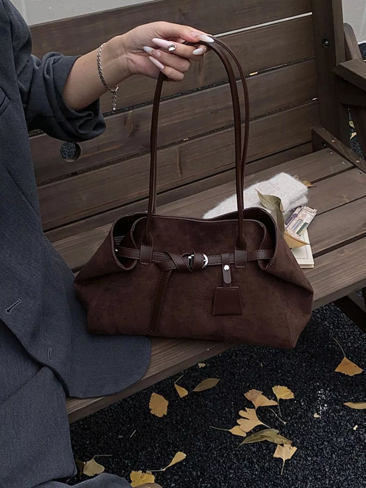 Brown suede shoulder bag with buckle strap, top handles, and front charm tag