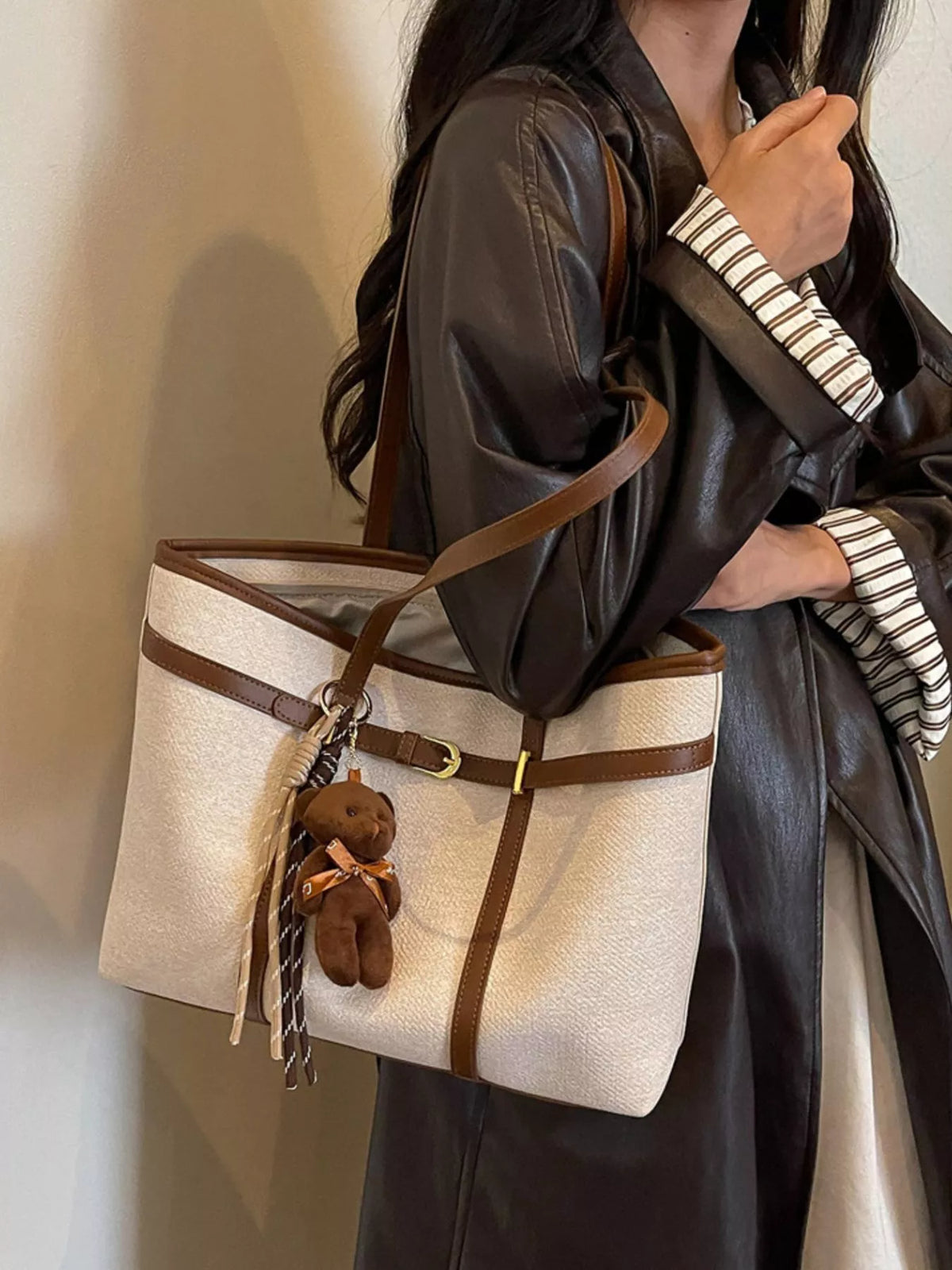 Off-white tote bag with brown handles, striped tassel, and teddy charm at front
