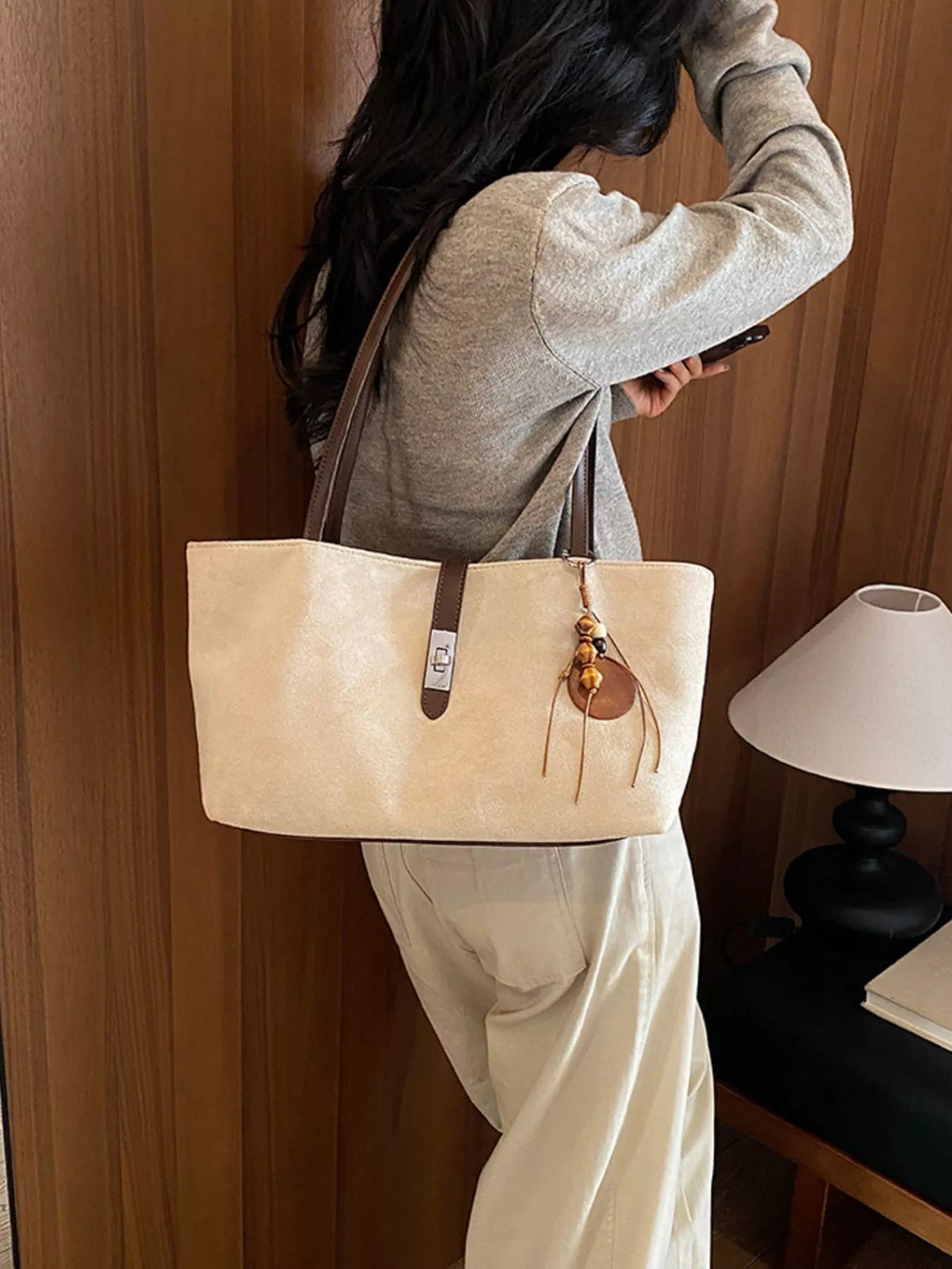 Beige suede tote bag on shoulder with vertical buckle strap and tassel charm