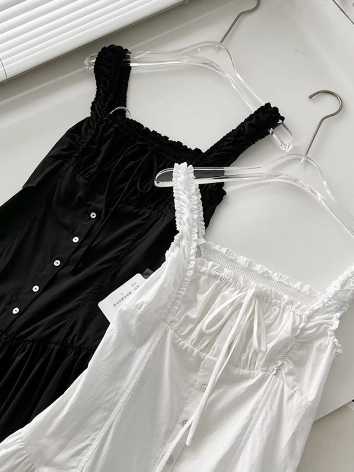 Black and white cotton maxi dresses on hangers with ruffled square necks and tie straps