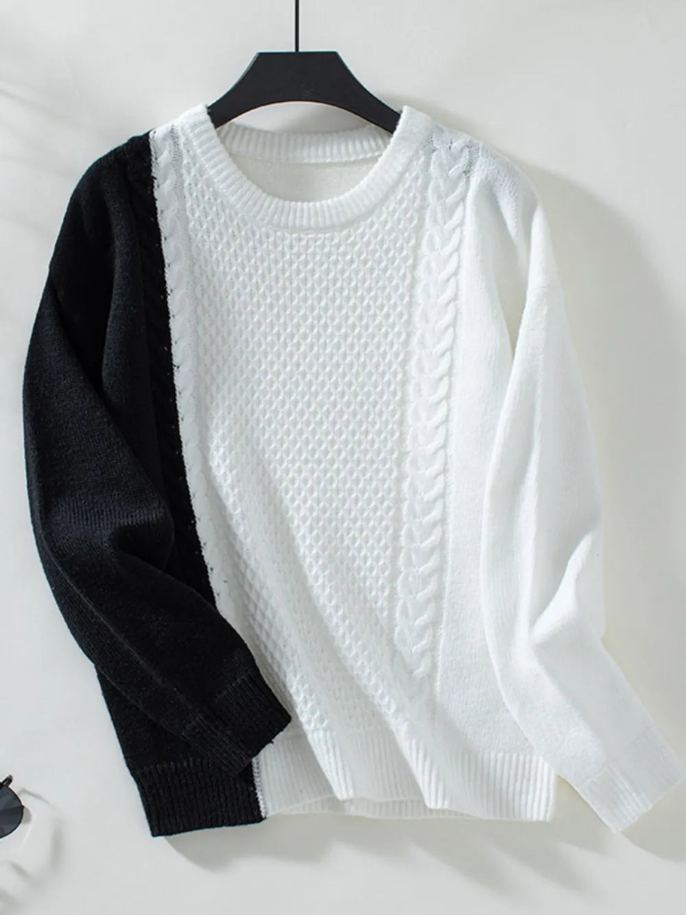 Two-tone cable knit round-neck sweater with white body and black sleeves on hanger