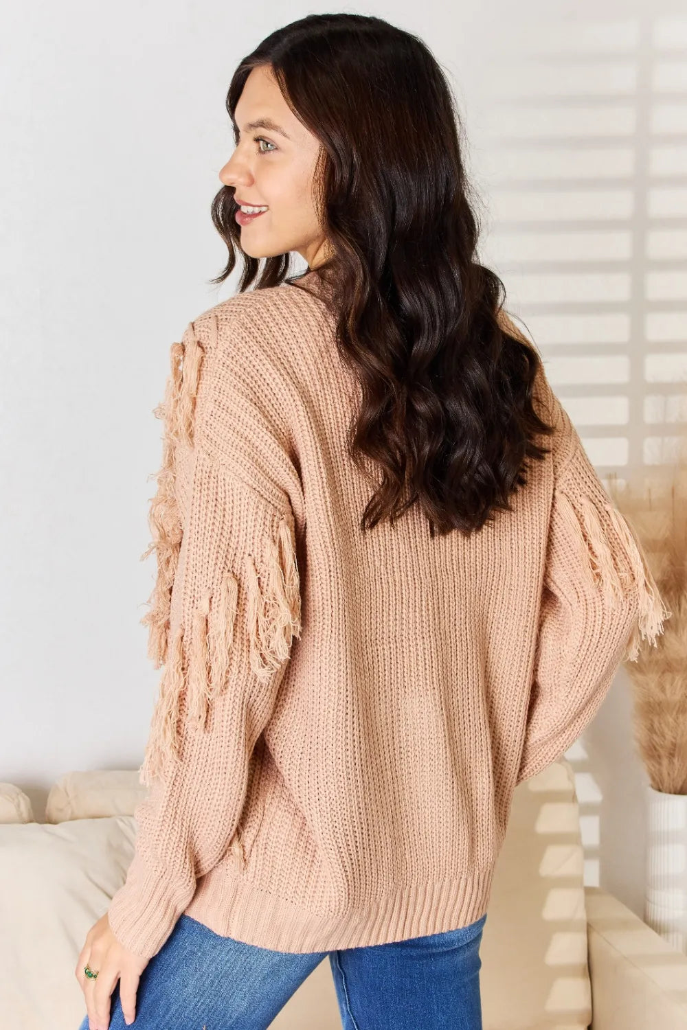 Dusty pink knit sweater with fringe tassel trim along one side sleeve