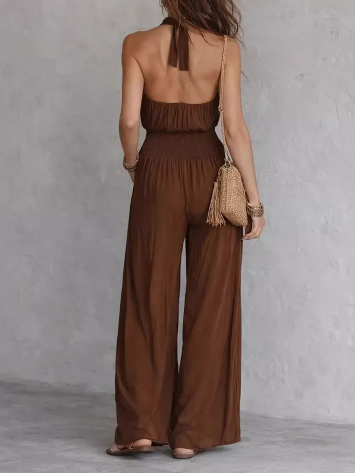 Brown open-back halter jumpsuit with smocked waist and wide-leg pants