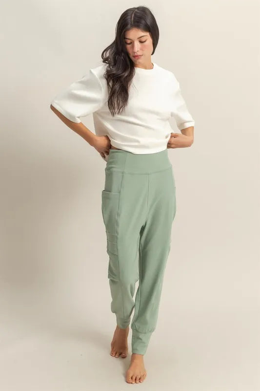 Sage green high-waist sweatpants with pocket detail and tapered cuffs