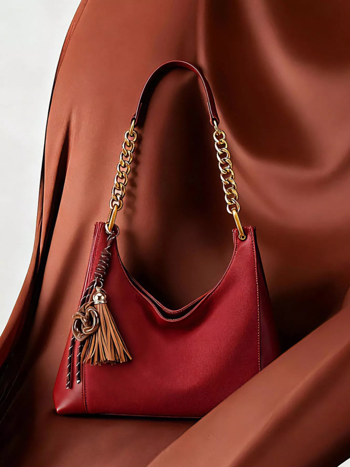 Wine red suede shoulder bag with chain handles and tassel charm, front pocket detail.