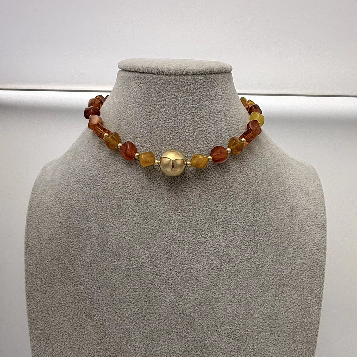 Gold-tone beaded necklace on gray bust with round center charm and amber bead mix