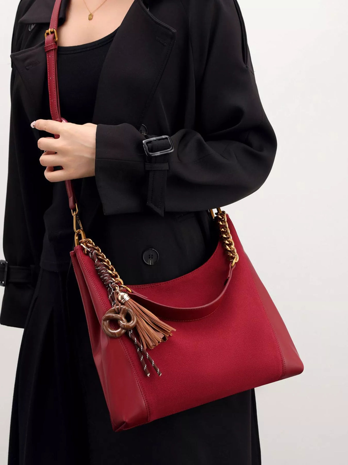 Wine red suede shoulder bag with chain strap and tassel charm, side view.