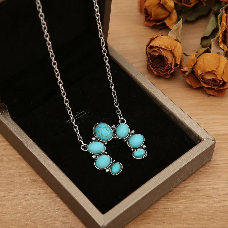 Turquoise oval stone pendant necklace with silver-tone chain, flower-shaped cluster.
