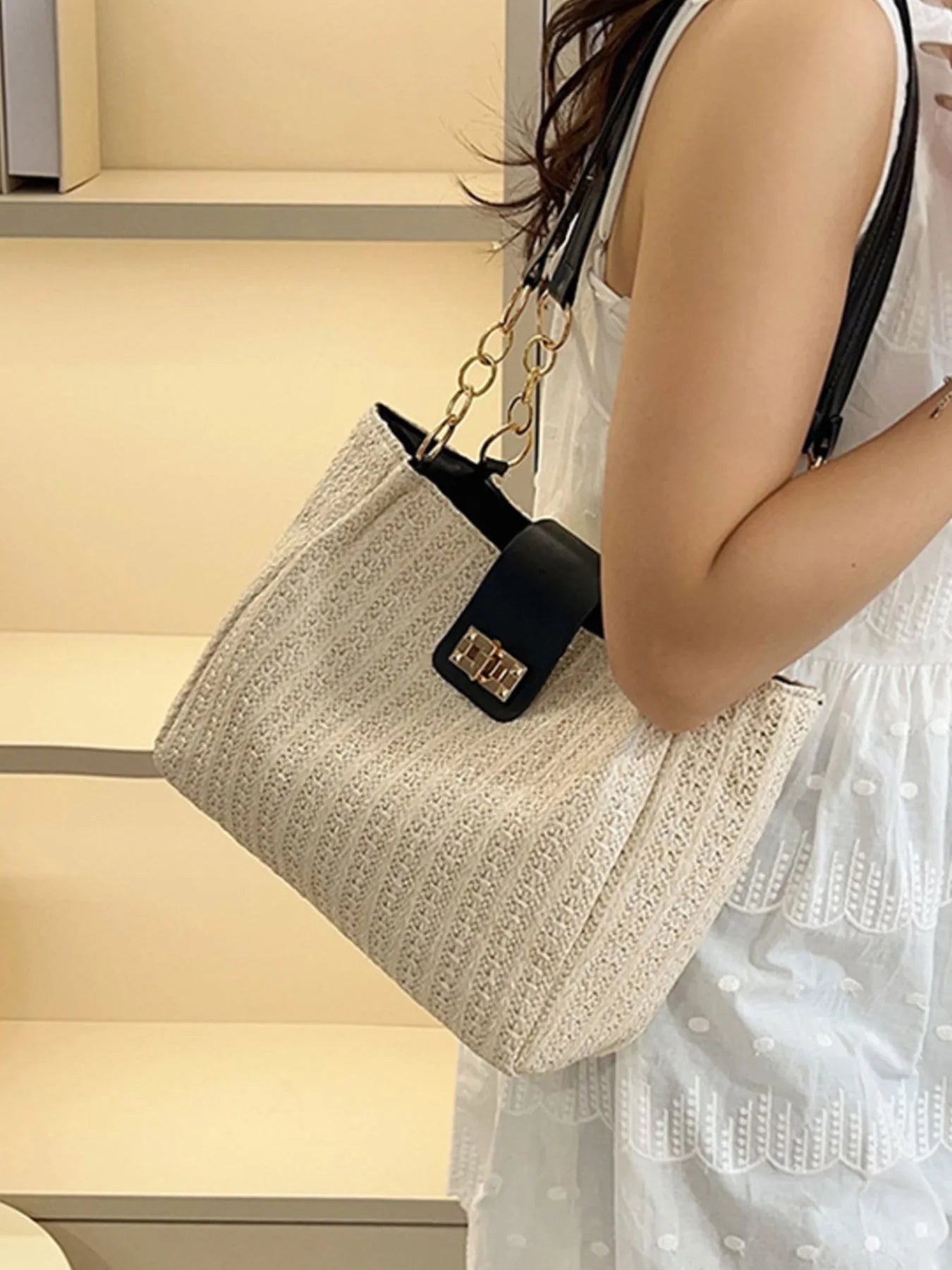 Beige woven straw shoulder bag with black strap, gold chain handle, and square clasp