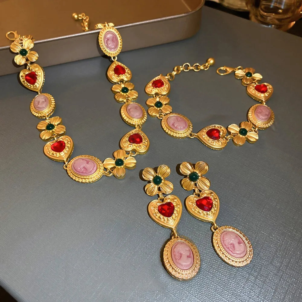 Gold-tone charm bracelet with red hearts, pink oval stones, and green teardrop details