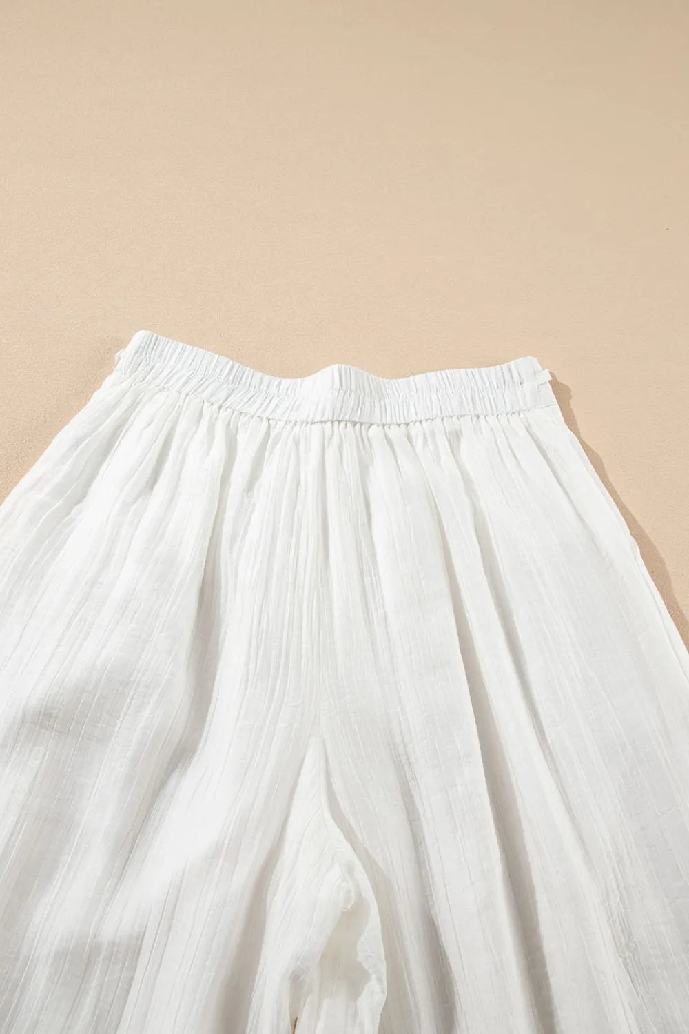 White pleated wide-leg pants with elastic waistband and gathered tie-waist top panel