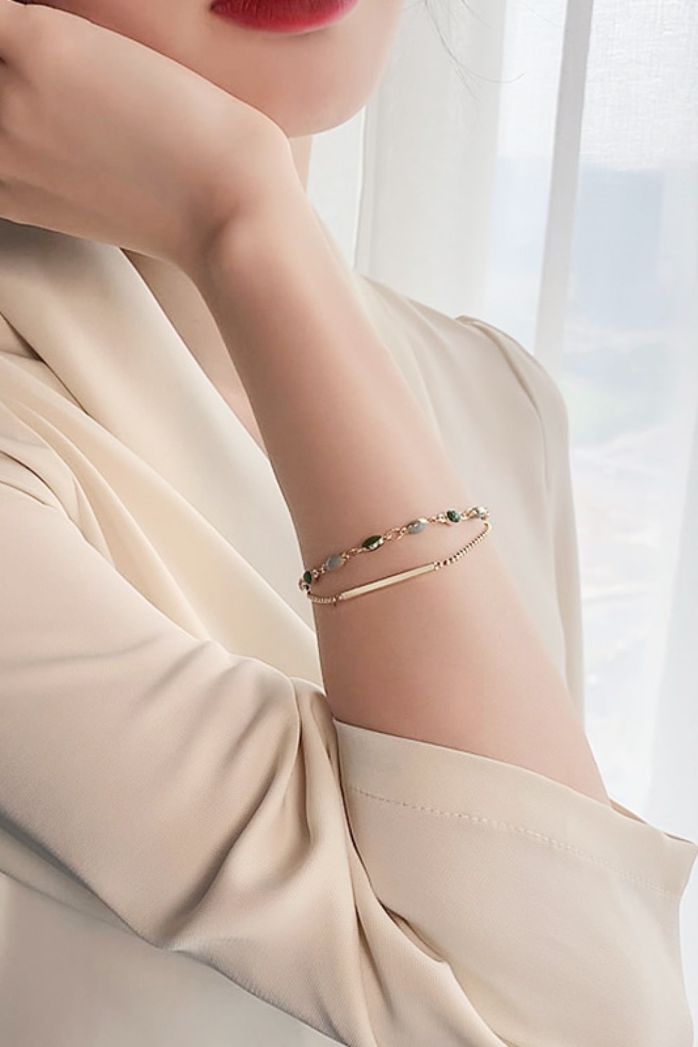 Double-layer gold-tone bracelet with green beads and gray accents on wrist
